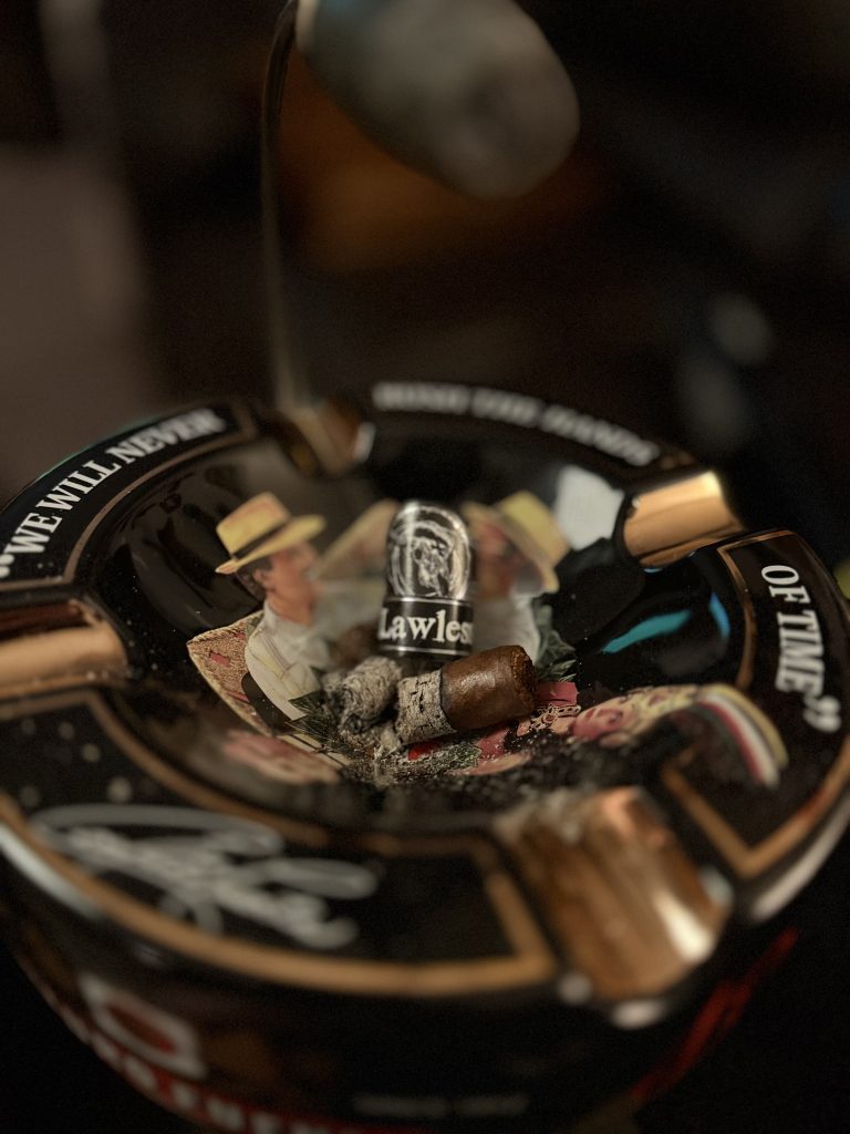 Finished Black Label Trading Co Lawless Robusto resting in an Arturo Fuente ashtray beside its removed Lawless cigar band